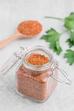 a jar filled with spices next to a wooden spoon and parsley sprigs