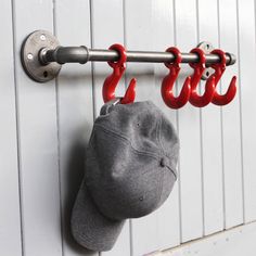 a baseball cap hanging from a hook on a white wall with red hooks attached to it