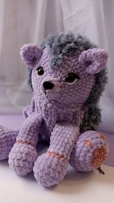 a crocheted purple stuffed animal sitting on top of a white table next to a curtain