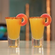 two glasses filled with orange juice and garnished with a pink donut on the rim