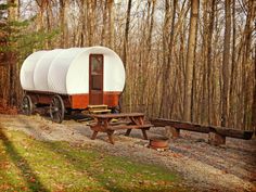 an old covered wagon is parked in the woods near picnic tables and benches on a gravel road