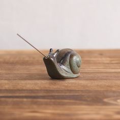 a small snail sitting on top of a wooden table next to a metal object with a stick in it's mouth