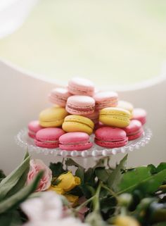 pink and yellow macaroons sitting on top of a cake stand next to flowers