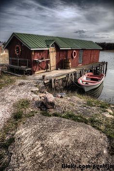 a boat is docked next to a small red house on the edge of a body of water