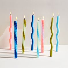 five candles are lined up in different colors and shapes, with one candle lit to the side