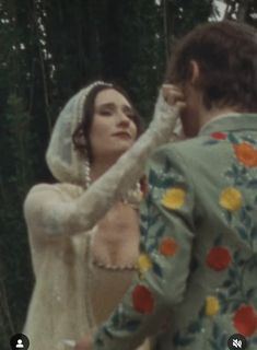 a man and woman dressed in wedding attire standing next to each other with trees in the background