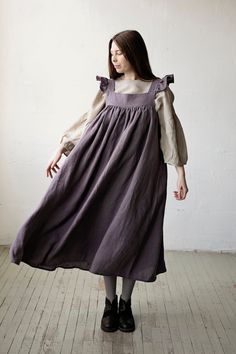 a woman in a purple dress standing on a wooden floor with her hands behind her back