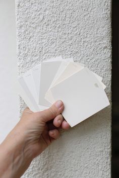 a hand holding some white cards against a wall