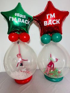 two snow globes with red, green and silver foil stars in them that say i'm back