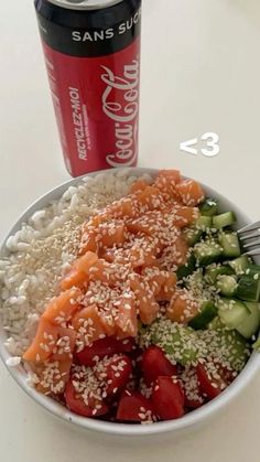 a white bowl filled with rice, cucumber and salmon next to a can of soda