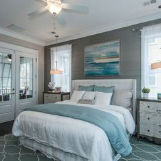 a bedroom with gray walls and white bedding, two windows, blue rugs and a painting on the wall