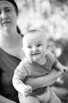 a black and white photo of a woman holding a baby in her arms while smiling at the camera