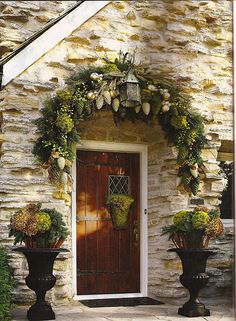 two large black planters sitting in front of a door with flowers on the side