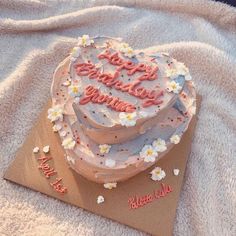 a heart shaped birthday cake sitting on top of a brown paper bag covered in white and pink frosting