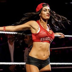 a female wrestler in a red top and black shorts is holding a rope with her right hand