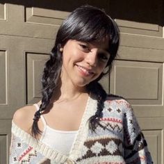 a woman standing in front of a garage door wearing a sweater and smiling at the camera