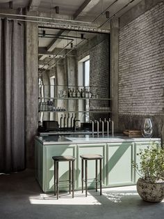 an industrial style kitchen with green cabinets and stools in front of a brick wall