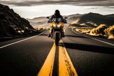 a person riding on the back of a yellow motorcycle down a curvy road