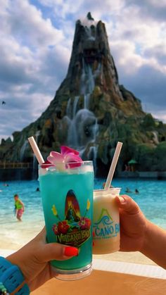 two people holding up drinks in front of a water fountain at the disneyland world resort