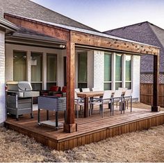 a patio with chairs, table and grill on the deck next to a house that has grass in front of it