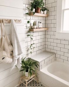 a white tiled bathroom with plants on the shelves and a bathtub in the corner