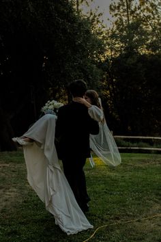 the bride and groom are walking through the grass in their wedding attire with veils over their heads