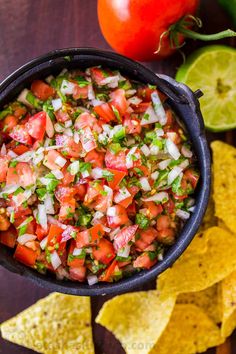 a black bowl filled with salsa surrounded by tortilla chips and lime wedges