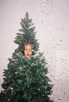 a woman peeking out from behind a christmas tree with snow falling all over her face