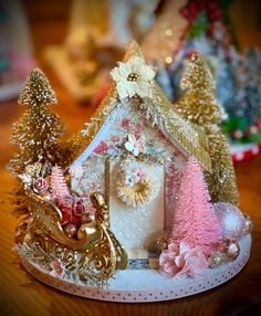 there is a small christmas house on top of a table with other ornaments around it