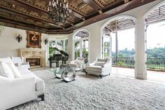 a large living room with white furniture and chandelier above the fireplace is shown