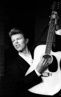 a man holding an acoustic guitar in his right hand and making a funny face while wearing a suit