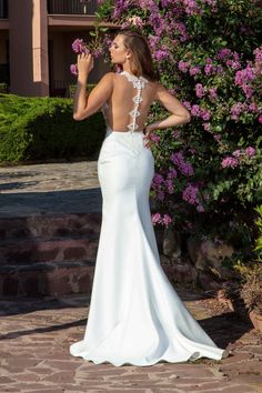 a woman in a white dress is standing near some purple flowers and looking at her back