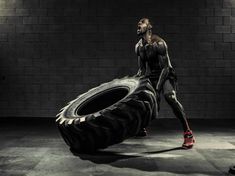 a man standing next to a giant tire in a dark room with bricks on the wall