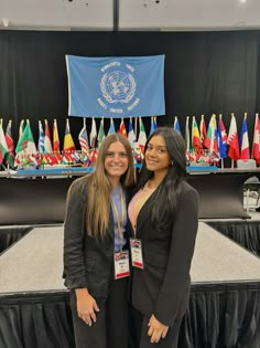 two women standing next to each other in front of a table with flags on it