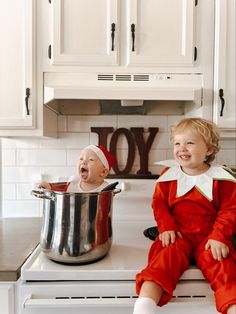 two babies are sitting on the stove and one is in a pot with his mouth open