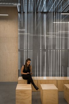 a woman sitting on top of wooden blocks in front of a wall with white lights