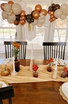 the table is set for thanksgiving dinner with balloons and flowers in vases on it