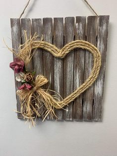 a heart shaped sign hanging on a wall with flowers in the center and rope attached to it