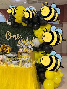 a table topped with lots of yellow and black balloons next to a sign that says one