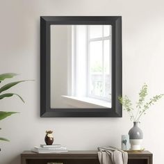 a mirror hanging on the wall above a table with a potted plant next to it