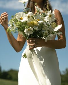 a woman in a white dress holding a bouquet of daisies and wildflowers