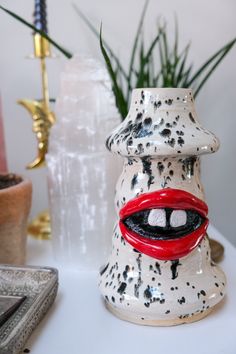 a ceramic vase with black and white speckles has red lips on it's mouth