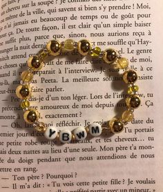 an open book with a beaded bracelet on it's side and words written in french