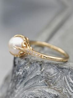 a pearl and diamond ring sitting on top of a rock