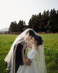 a bride and groom kissing in the middle of a field with trees in the background