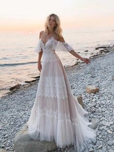 a woman standing on top of a beach next to the ocean wearing a white dress