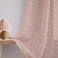 a lamp on a table next to a pink curtain with white flowers in the background