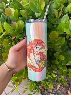 a hand holding a disney princess tumbler next to green leaves