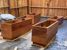 three wooden planters sitting on top of a stone floor next to a fence and rock wall