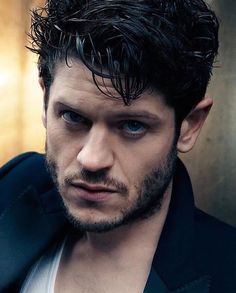 a man with dark hair and blue eyes looks at the camera while wearing a suit